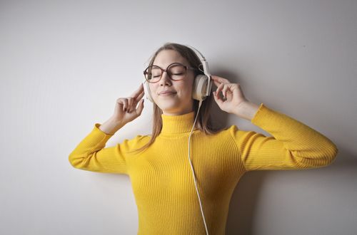 Free Woman in yellow sweater smiles while listening to music with headphones, eyes closed. Stock Photo