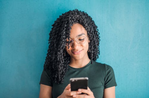 Portrait Photo of Smiling Woman in Black T-shirt and Glasses Using Her Smartphone