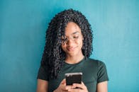 一位戴着眼镜、面带微笑的女性，在充满活力的蓝色背景下使用手机