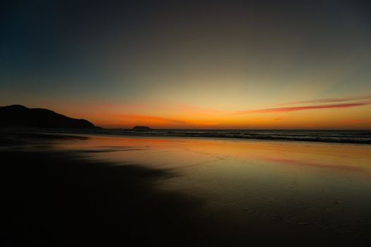 Serene beach sunset with vivid orange and blue hues reflecting on the water and shore.