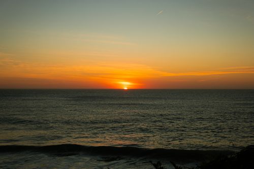 Free A serene sunset over the ocean with vibrant orange and yellow hues reflecting on the water. Stock Photo