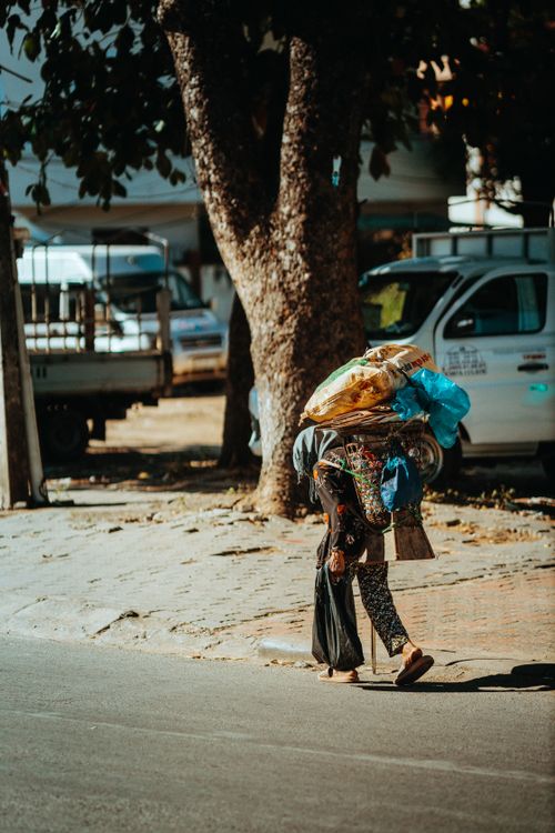 Free A person carrying goods on a busy urban street under the shade of trees in Kon Tum, Vietnam. Stock Photo