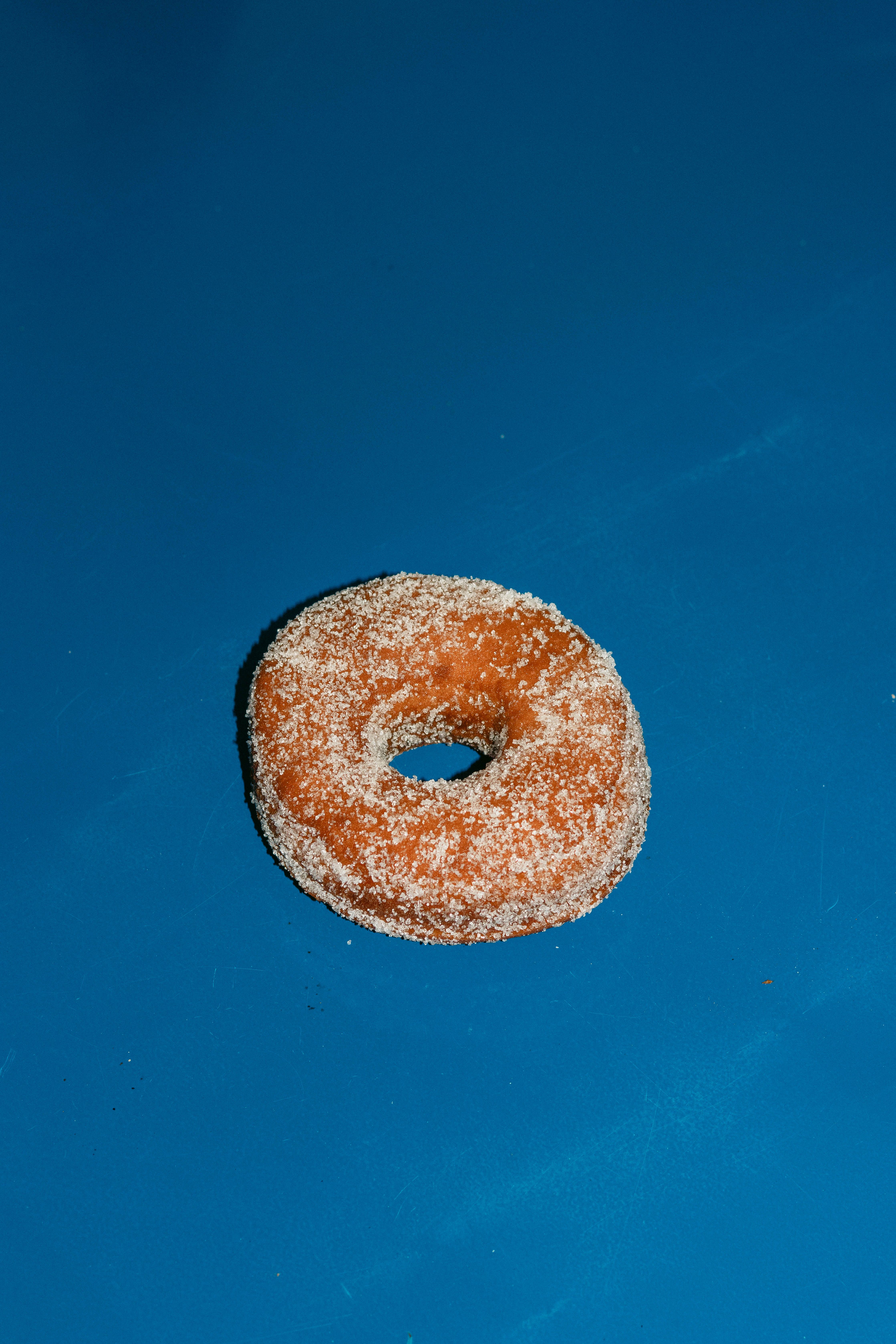 A delicious sugar-coated donut placed on a vibrant blue surface, photographed from above.