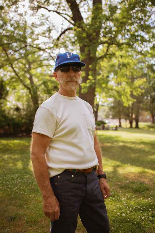 Free Man in casual attire stands outdoors in a sunny park setting. Stock Photo