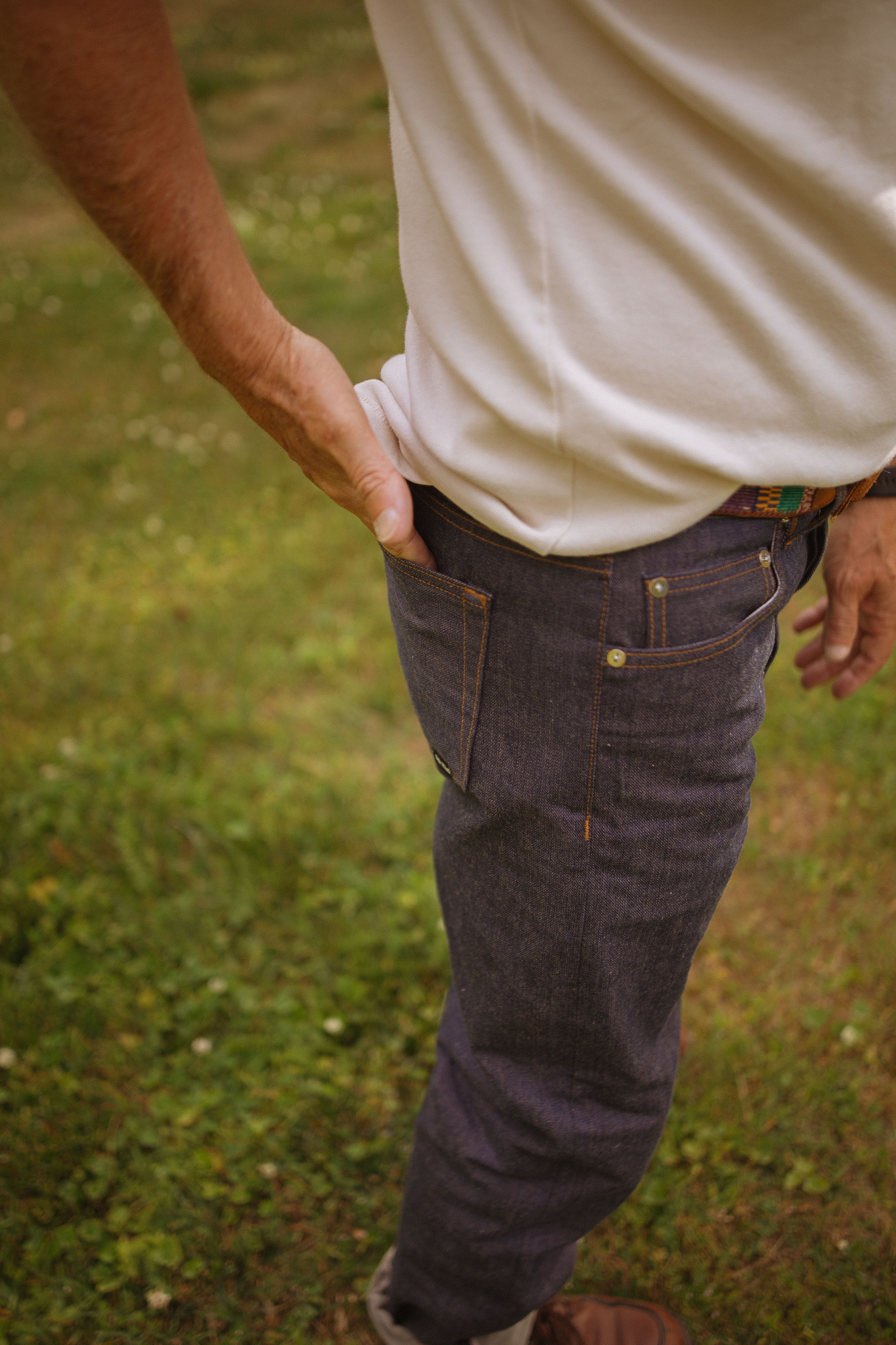 Man wearing denim jeans and white t-shirt in a natural outdoor setting, showcasing casual style.