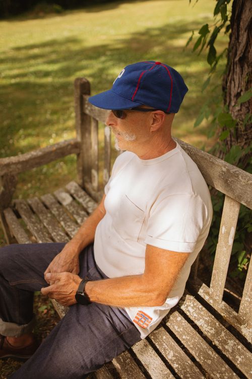 Free Relaxed outdoor portrait of a man in a white t-shirt and blue cap sitting on a bench. Stock Photo