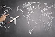 Top view of miniature airplane placed on over gray world map with crop hand of anonymous person indicating direction representing travel concept