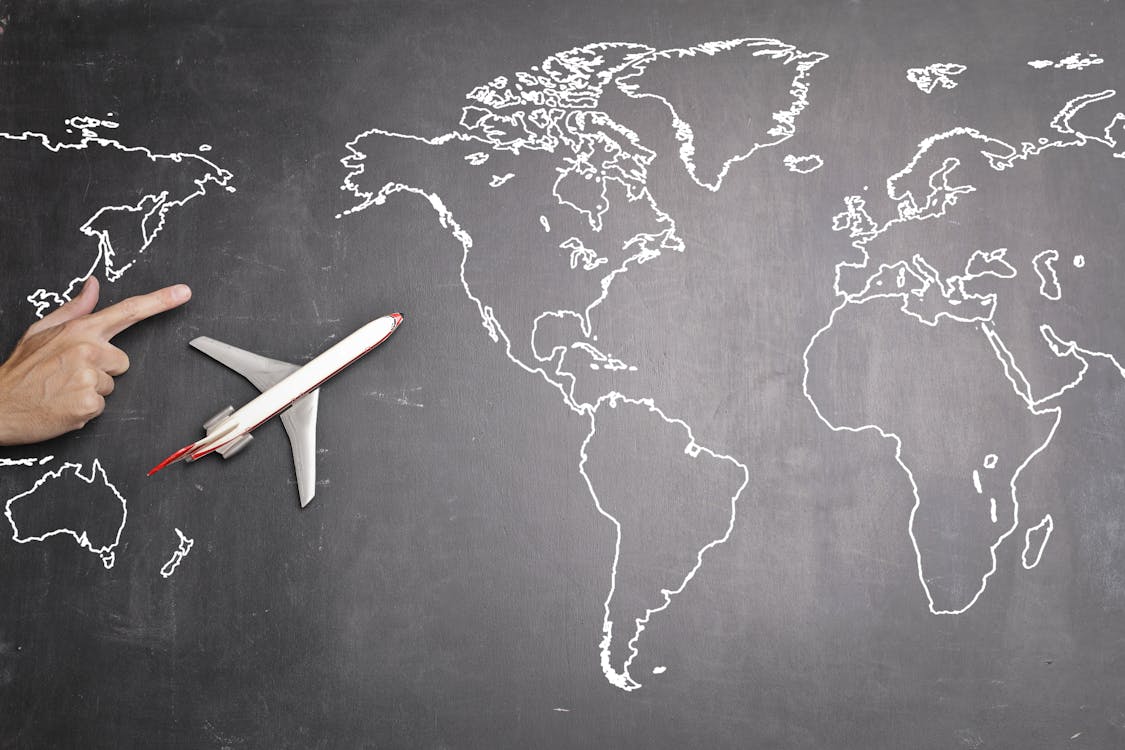 Free Top view of miniature airplane placed on over gray world map with crop hand of anonymous person indicating direction representing travel concept Stock Photo