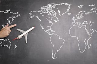 Top view of miniature airplane placed on over gray world map with crop hand of anonymous person indicating direction representing travel concept