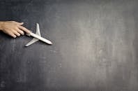 Top view of crop anonymous person driving toy airplane on empty blackboard while representing journey concept