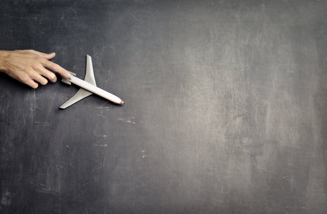 Free Top view of crop anonymous person driving toy airplane on empty blackboard while representing journey concept Stock Photo
