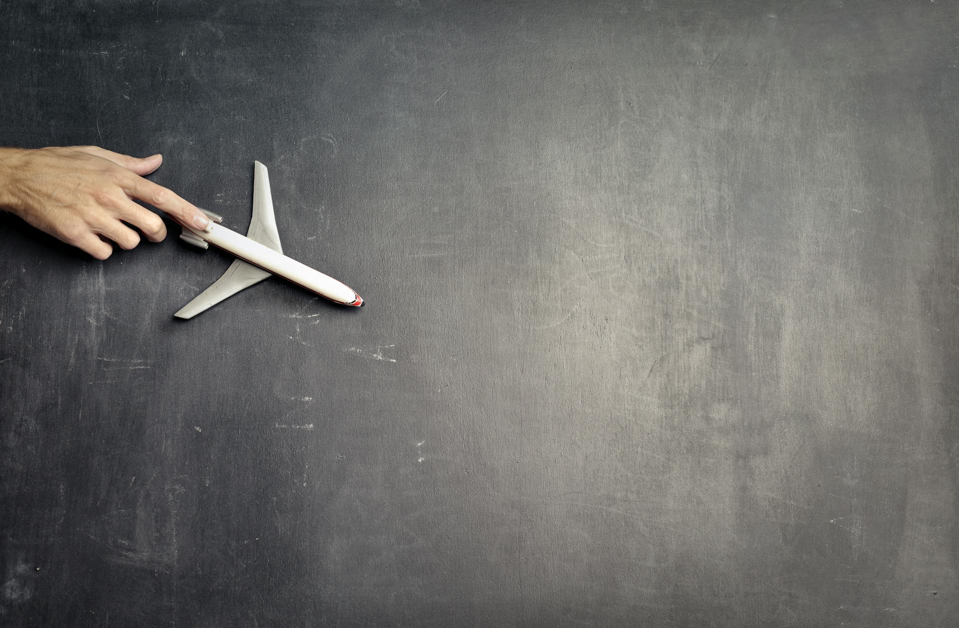 Top view of crop anonymous person driving toy airplane on empty blackboard while representing journey concept