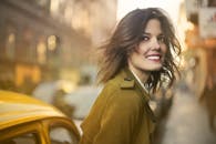 穿着外套的微笑女人在阳光明媚的城市街道上散步