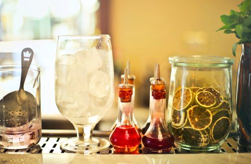 Free Wineglass with ice cubes for cocktail placed on counter near glass jars with colorful syrups and dried citrus slices Stock Photo