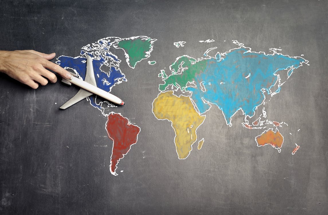 Free Top view of crop anonymous person holding toy airplane on colorful world map drawn on chalkboard Stock Photo
