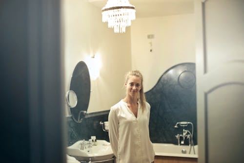 Photo of Smiling Woman in A White Silk Top Standing in a Bathroom