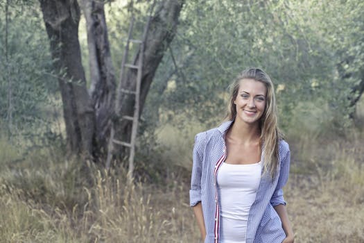 一位穿着休闲装的女子面带微笑，站在树木和草地之间，散发着自然之美