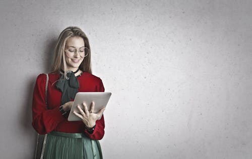 Foto Di Donna Sorridente In Camicia A Maniche Lunghe Rossa E Vestito Verde Utilizzando Un Tablet