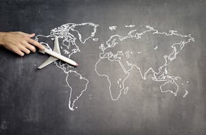 From above of crop anonymous person driving toy airplane on empty world map drawn on blackboard representing travel concept