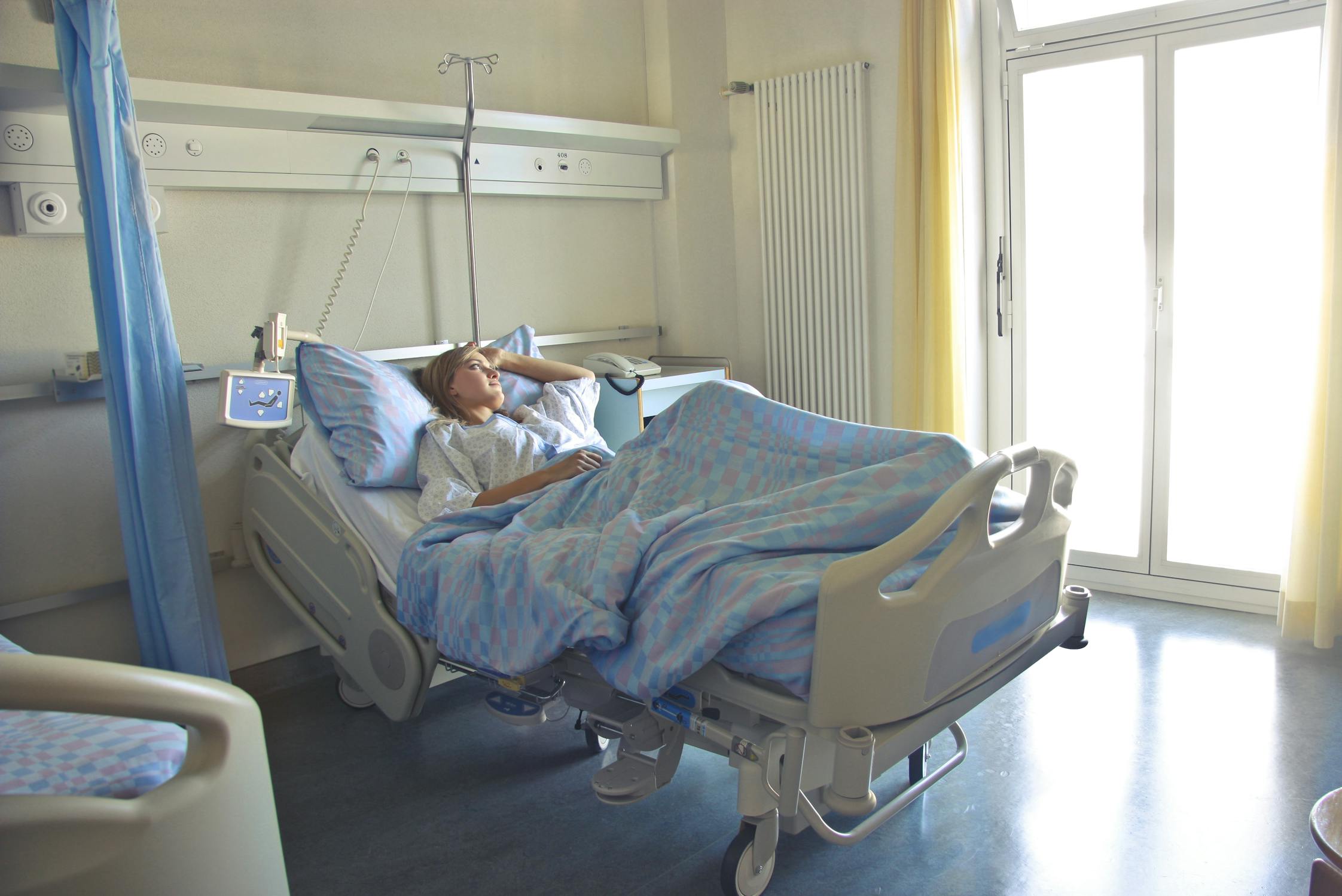 A woman lays in a hospital bed staring out the window