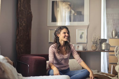 Photo of Laughing Woman in Pink Long Sleeve Shirt and Blue Denim Jeans Sitting on Red Sofa Chair