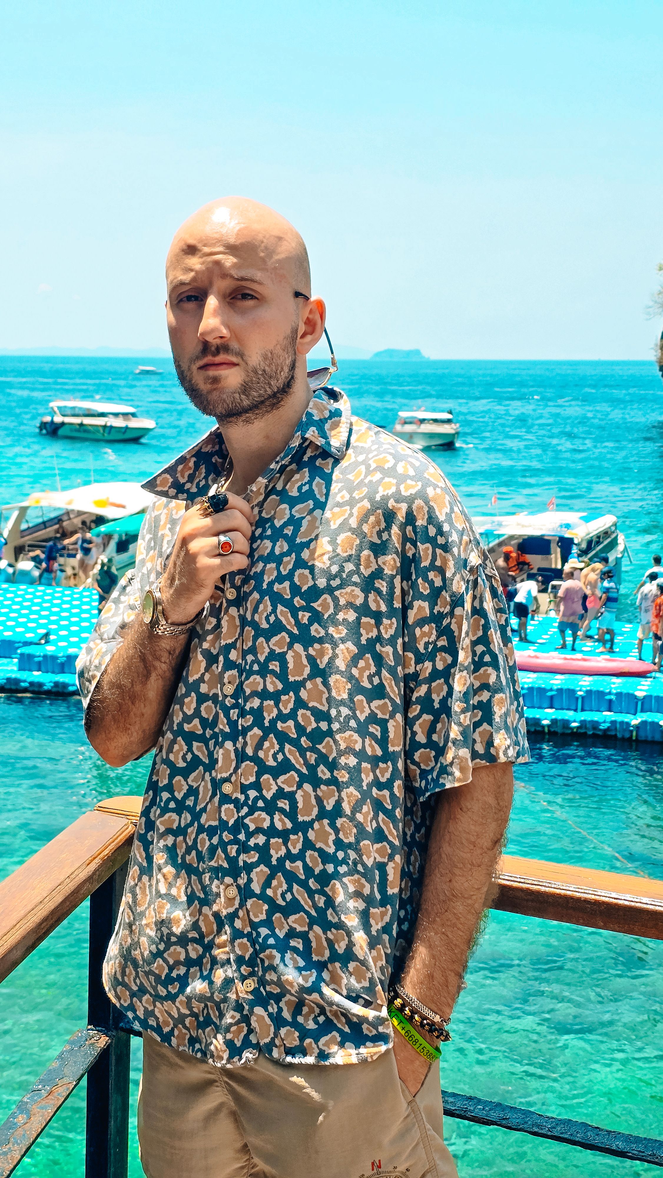 A man stands on a balcony overlooking a vibrant seaside with boats and swimmers.