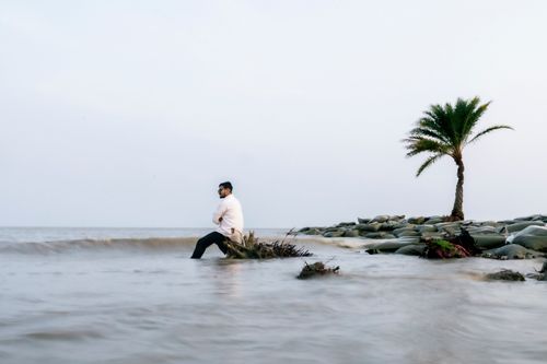 Free A peaceful scene of a person sitting by the ocean near a solitary palm tree. Stock Photo