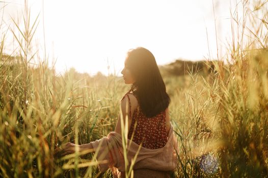 A peaceful moment as a woman walks through a sunlit field surrounded by tall grass in the golden hour.