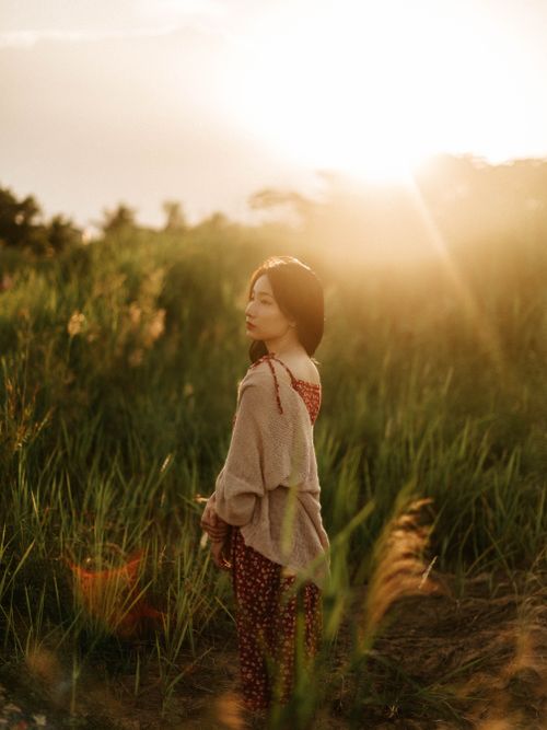 Free Young woman stands in a sunlit field at sunset, evoking serenity and natural beauty. Stock Photo