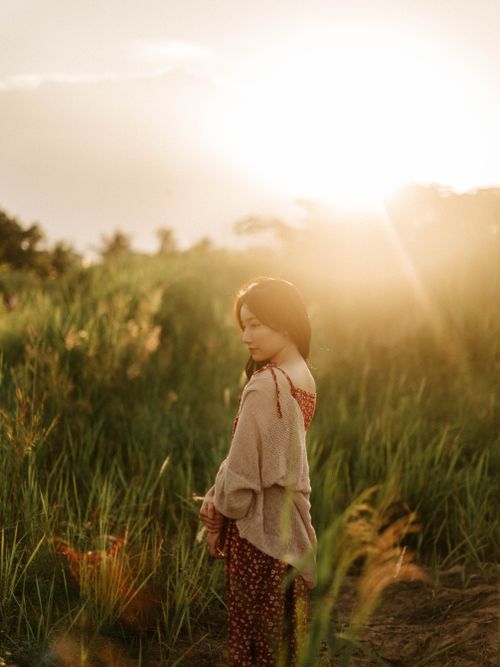 Free A woman stands peacefully in a sunlit grassy field during golden hour. Stock Photo