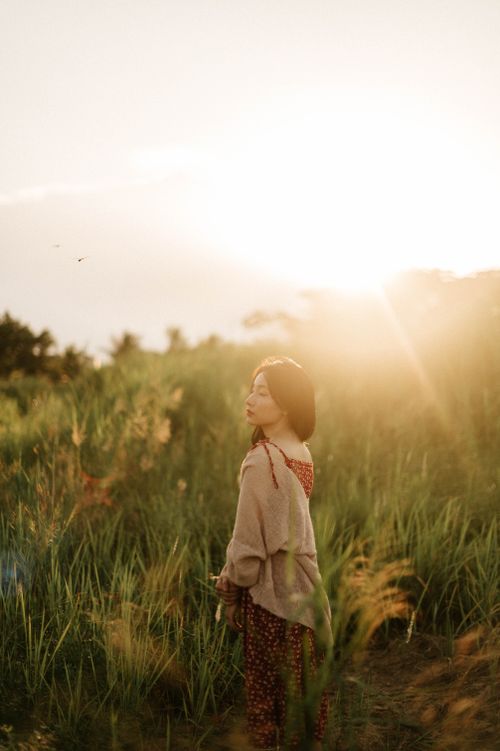 Free A woman stands peacefully in a sunlit meadow, bathed in the warm glow of golden hour. Stock Photo