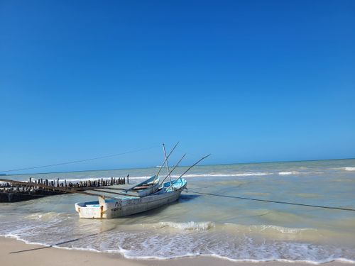 Free A serene scene of a traditional fishing boat on a tropical beach under clear blue skies. Stock Photo