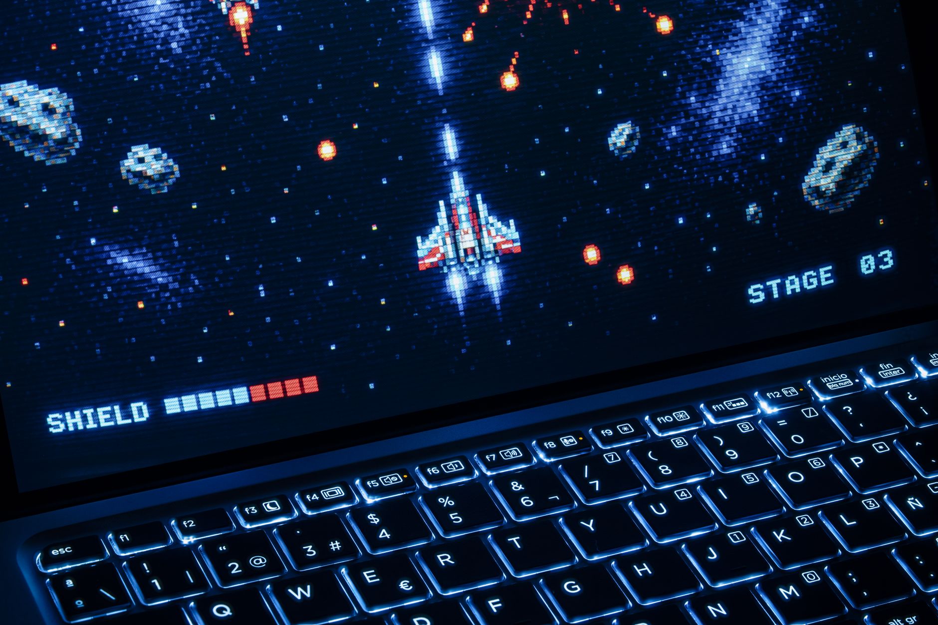A classic arcade space shooter game displayed on a laptop with illuminated keyboard, showing retro graphics.