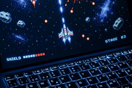 A classic arcade space shooter game displayed on a laptop with illuminated keyboard, showing retro graphics.