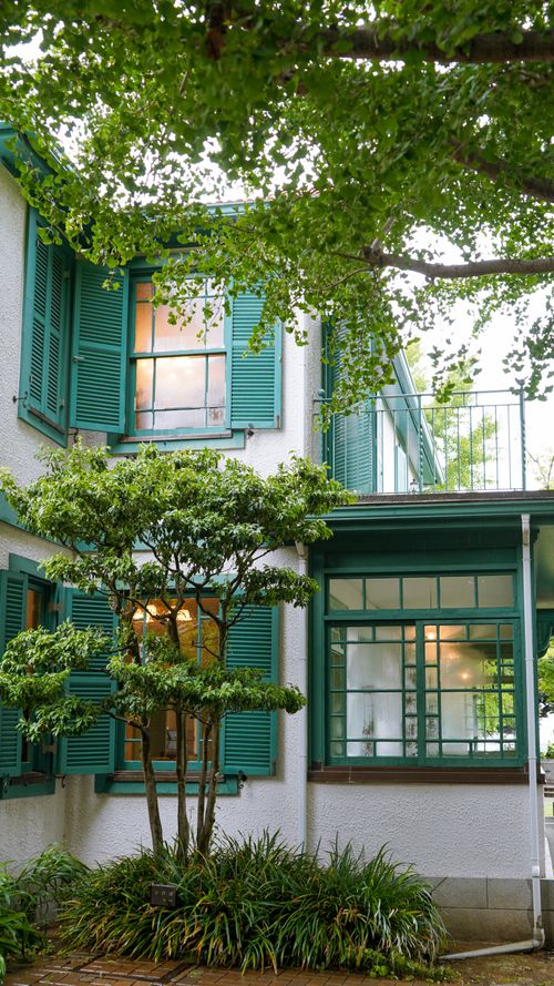 Free A serene view of a traditional Japanese house with green shutters and lush garden. Stock Photo