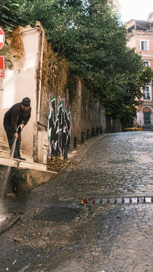Free Man cleaning a graffiti-covered cobblestone street with a hose in urban setting. Stock Photo