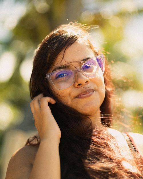 Free Portrait of a young woman with glasses under natural sunlight, showcasing a warm and relaxed expression. Stock Photo