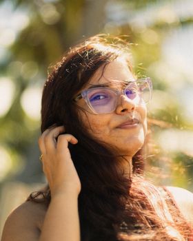 Candid portrait of a smiling woman in glasses enjoying the sunlight outdoors, creating a tropical feel.