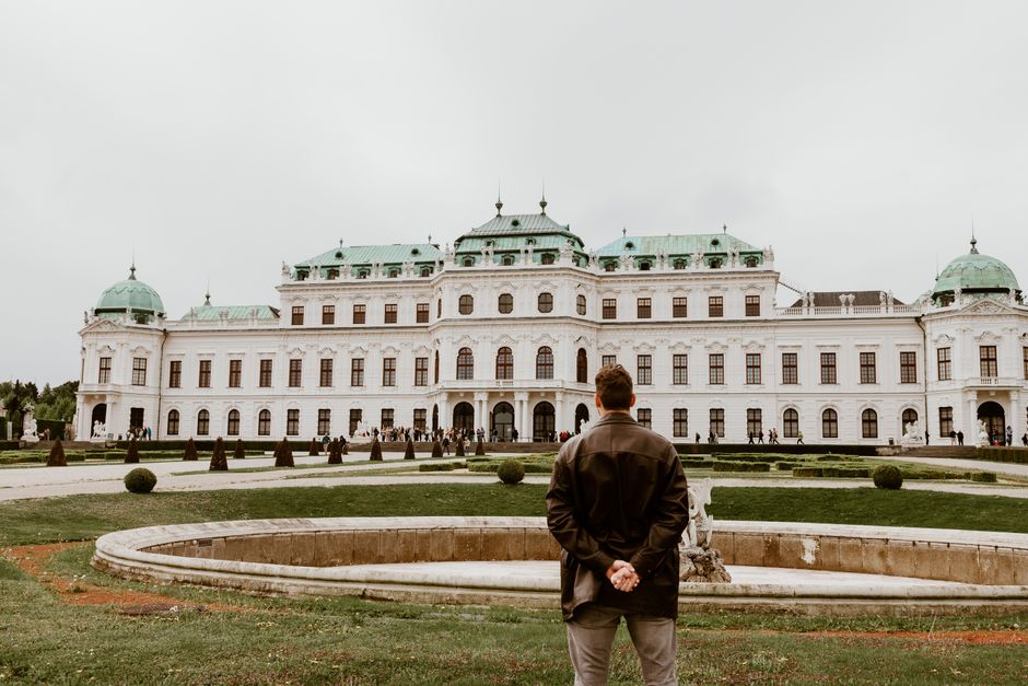 A man stands in front of the Belvedere Palace in Vienna, Austria, during a cloudy day.