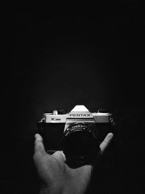 Free A vintage Pentax K1000 film camera held against a dark background. Stock Photo