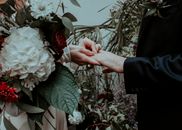 Crop bride with gorgeous flower bouquet putting wedding ring on finger of groom on wedding ceremony