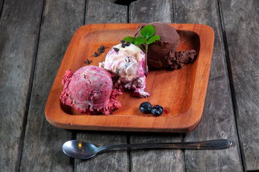 Three artisanal ice cream scoops on a wooden plate with chocolate chips and blueberries.