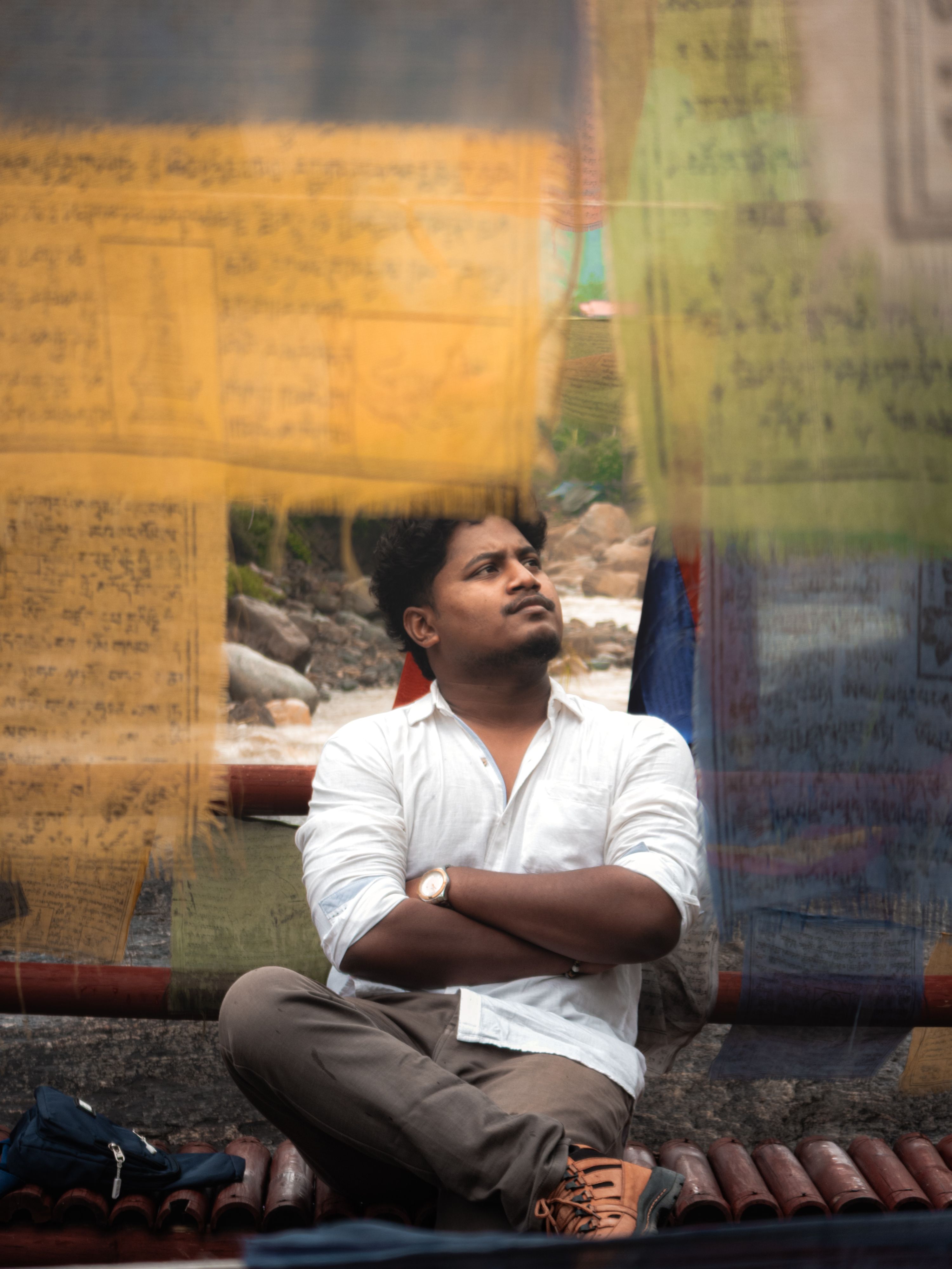 A man sitting contemplatively among colorful prayer flags, suggesting introspection and peace.