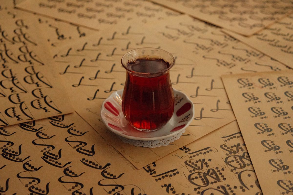 Arabic calligraphy practice sheets beside a glass of tea