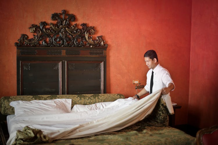 Male Servant Making Bed In Luxury Hotel Room