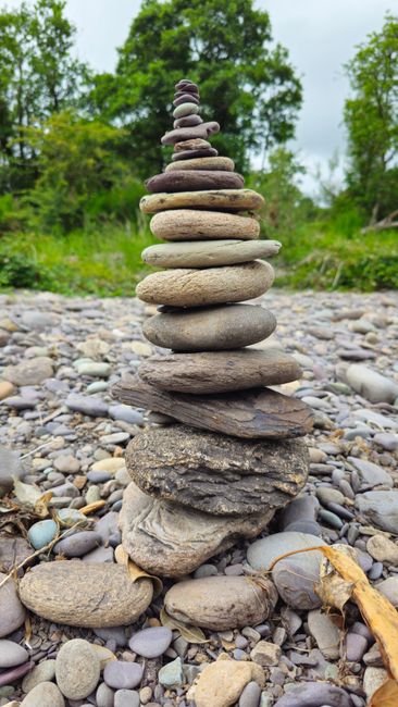 Fotomural Un mojón de piedras en perfecto equilibrio sobre una playa de guijarros rodeada de exuberante vegetación.