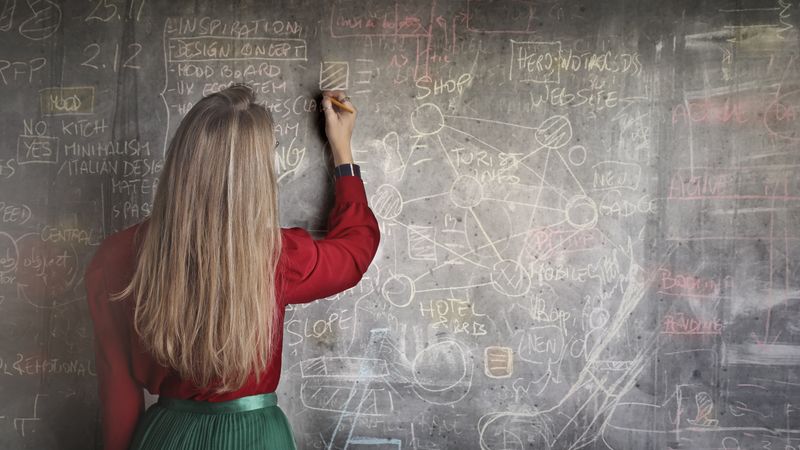 Person drawing and writing on a large chalkboard full of marks