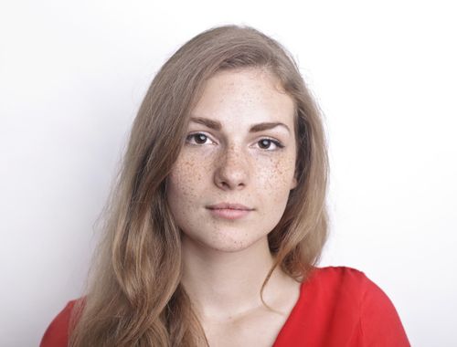 Free Portrait of a young woman with freckles wearing a red top against a white background. Stock Photo