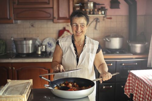 Free A cheerful woman cooking a meal in a cozy, rustic kitchen setting. Stock Photo
