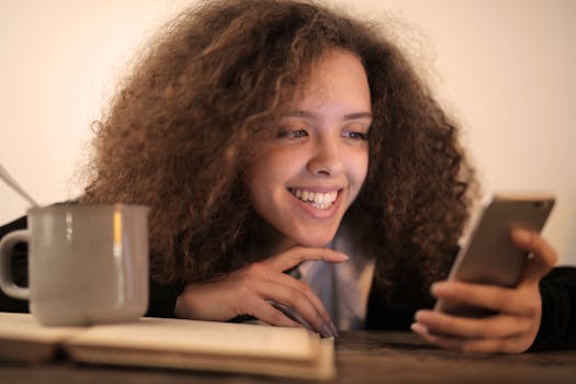 A cheerful woman with curly hair smiles while texting on her smartphone.